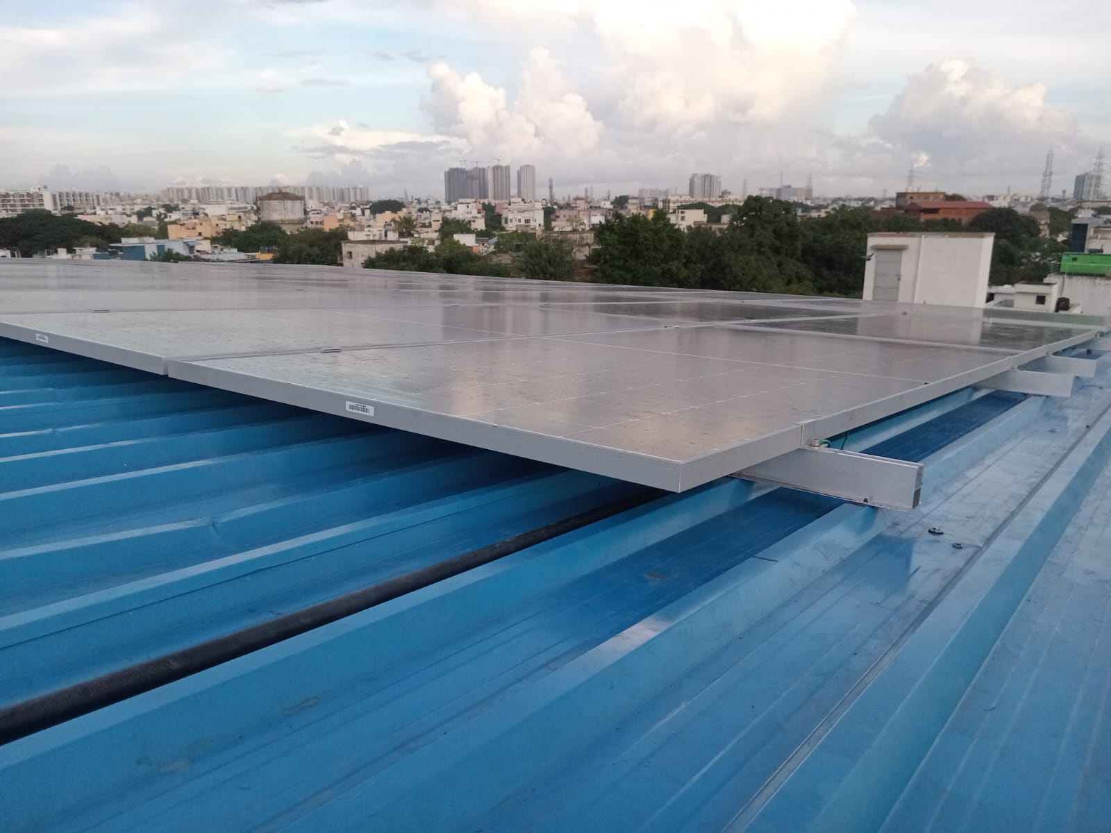 Commercial solar panel installation on industrial blue metal roof with urban cityscape background